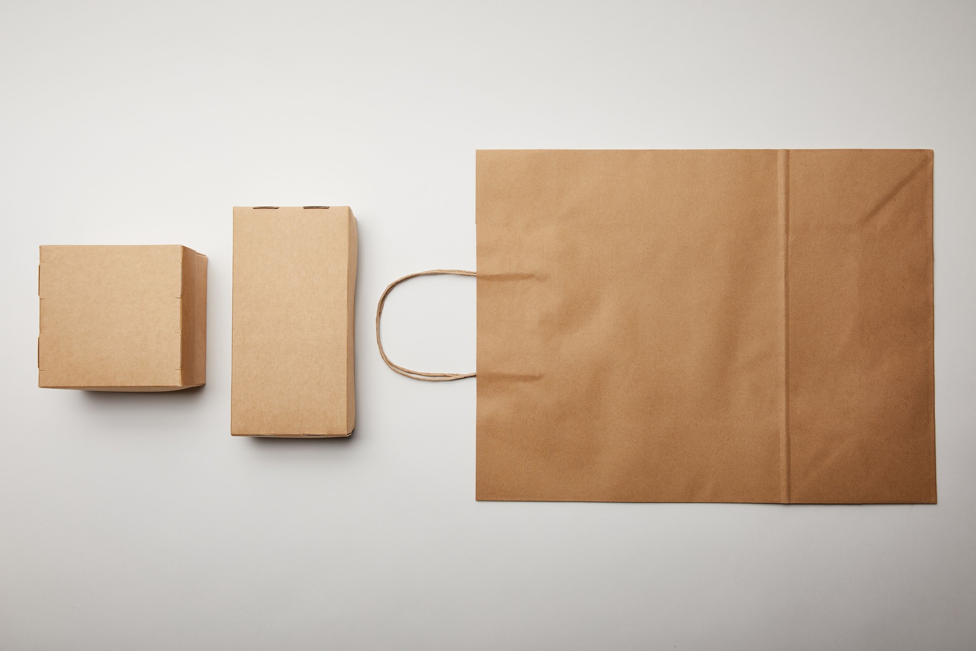 elevated view of arranged view of cardboard boxes and food delivery paper bag on white surface, minimalistic concept